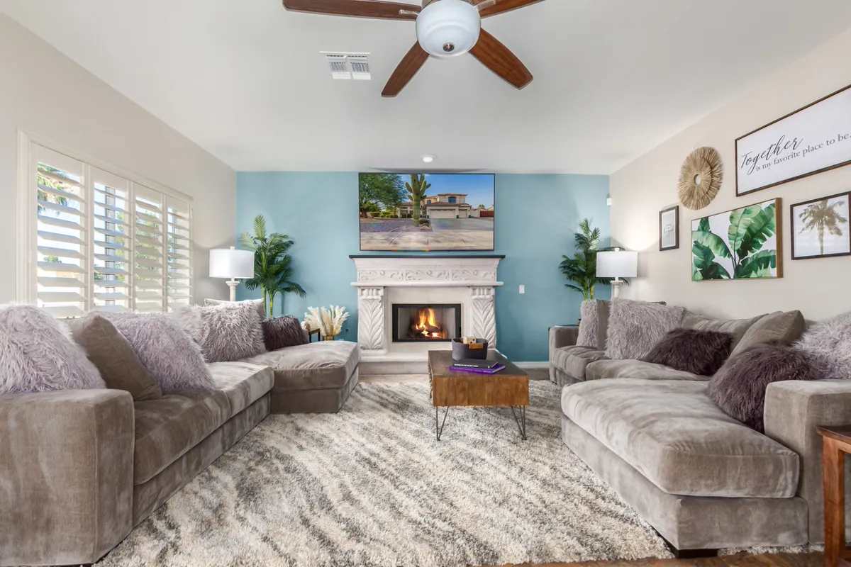 A spacious living room featuring a large sectional sofa arranged around a modern fireplace with a TV above it. The room is decorated with tasteful wall art and potted plants, and the overall ambiance is cozy and welcoming—ideal for gatherings and relaxing after a busy day.