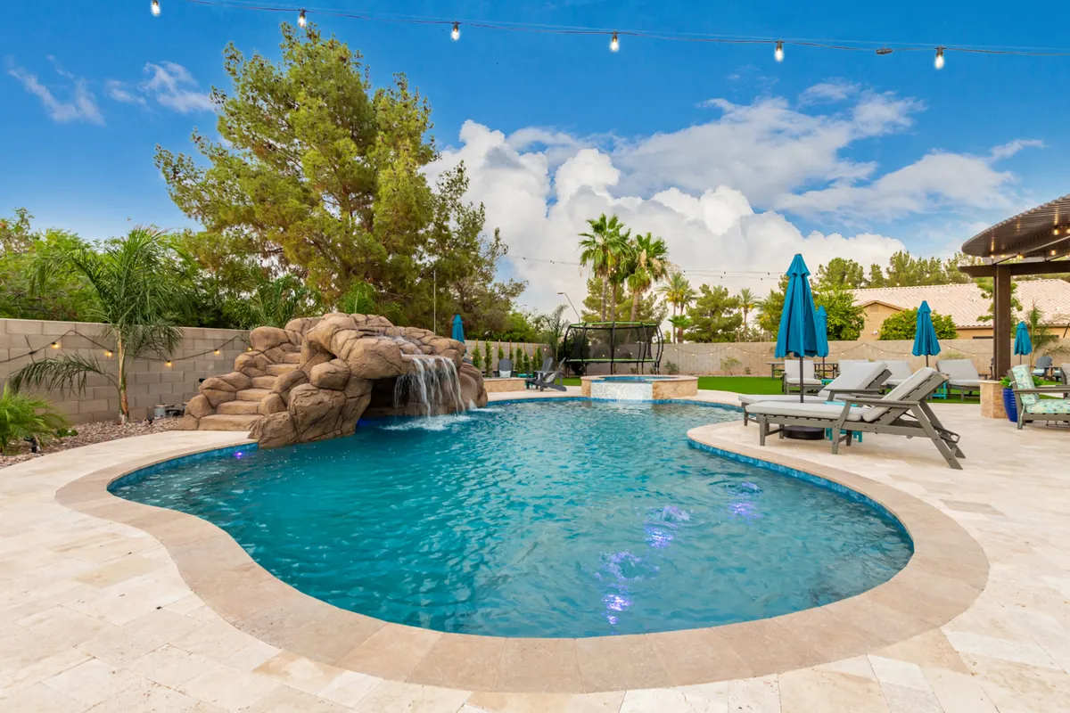 A wide view of the property’s swimming pool area, complete with a cascading waterfall, inviting lounge chairs, a shaded patio, and ambient string lights. The scene exudes a welcoming atmosphere perfect for group relaxation and evening gatherings under the Arizona sky.