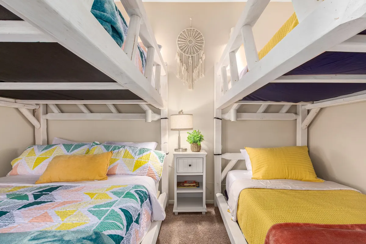 A playful and cozy bedroom with bunk beds, colorful bedding, a nightstand with a lamp, and a dreamcatcher hanging above. The space is designed for relaxation and fun, ideal for children or groups seeking a memorable stay.